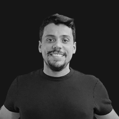Smiling man with short dark hair and beard wearing a black t-shirt on a black background.
