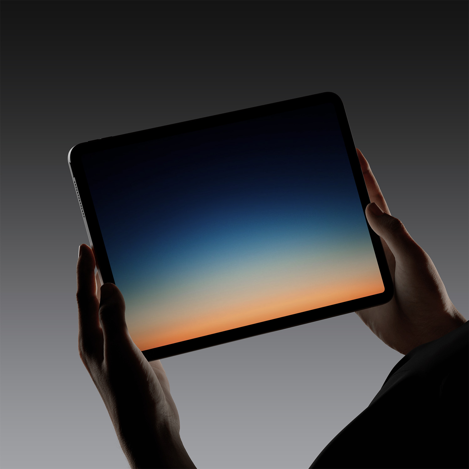 Hands holding a tablet with a gradient screen showing dark blue to orange fading colors.