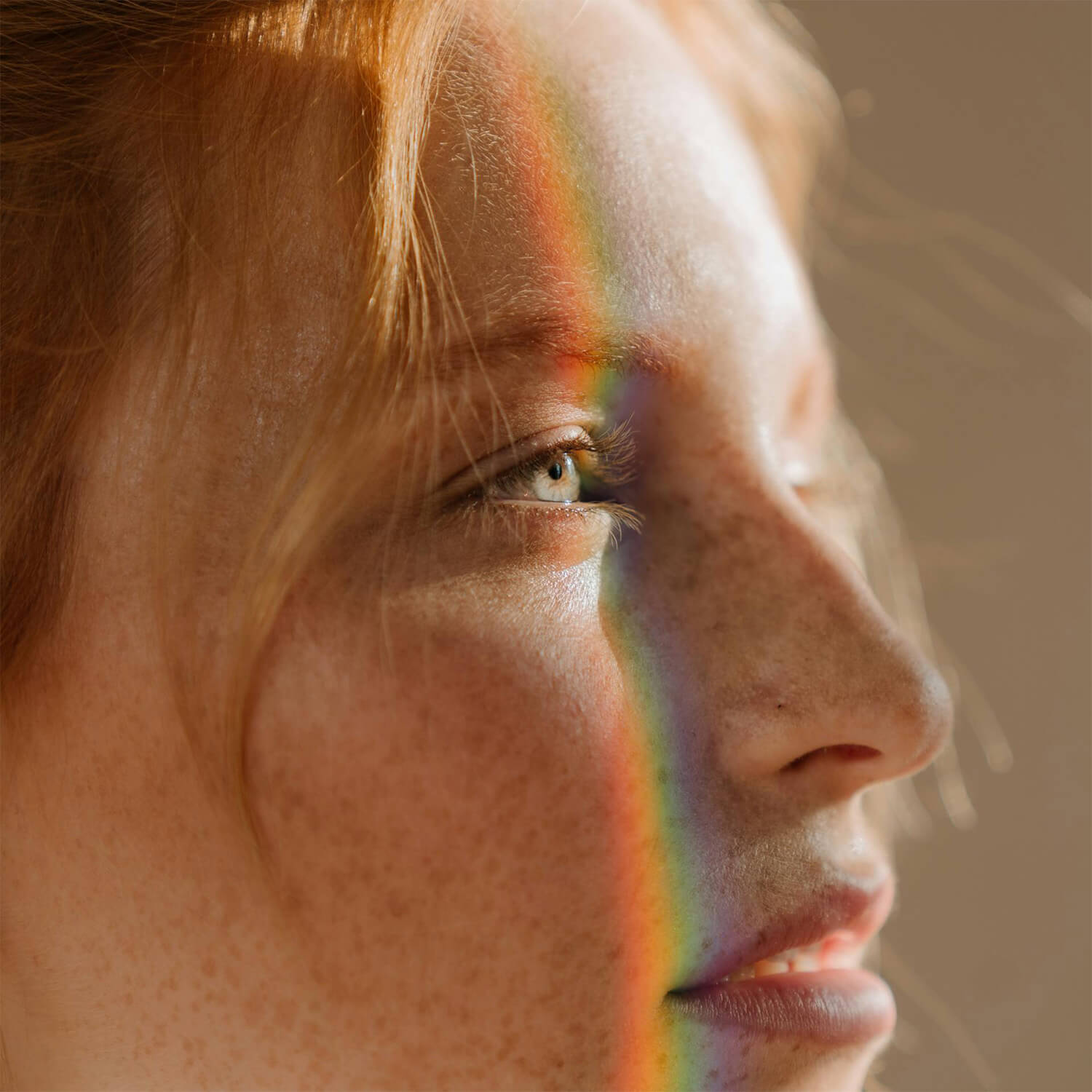 Close-up of a red-haired woman’s face with freckles and a rainbow light across her cheek and eye.